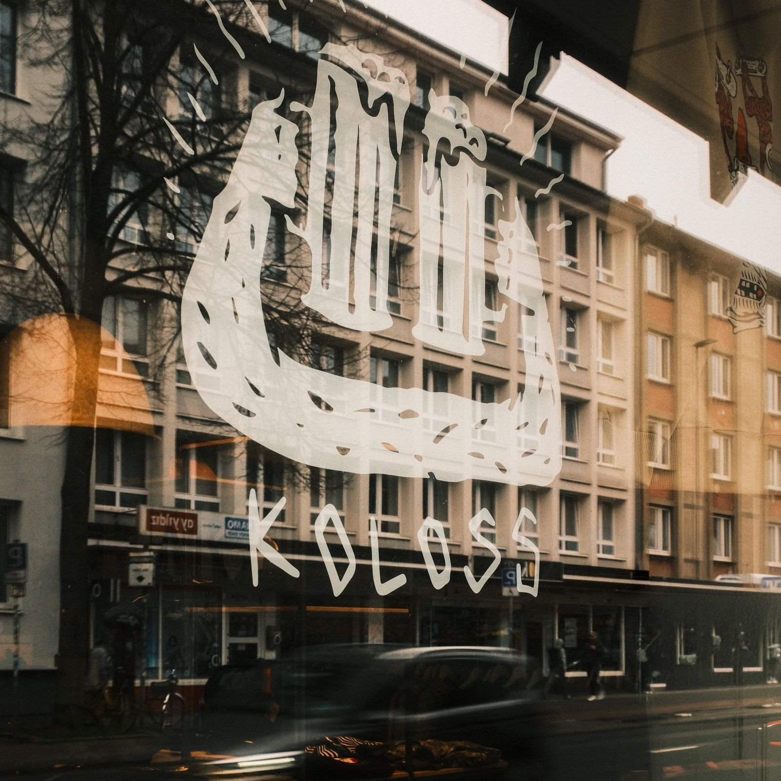 Koloss-Logo in der Fensterscheibe des Black Heaven Skateshops, dahinter die Straße